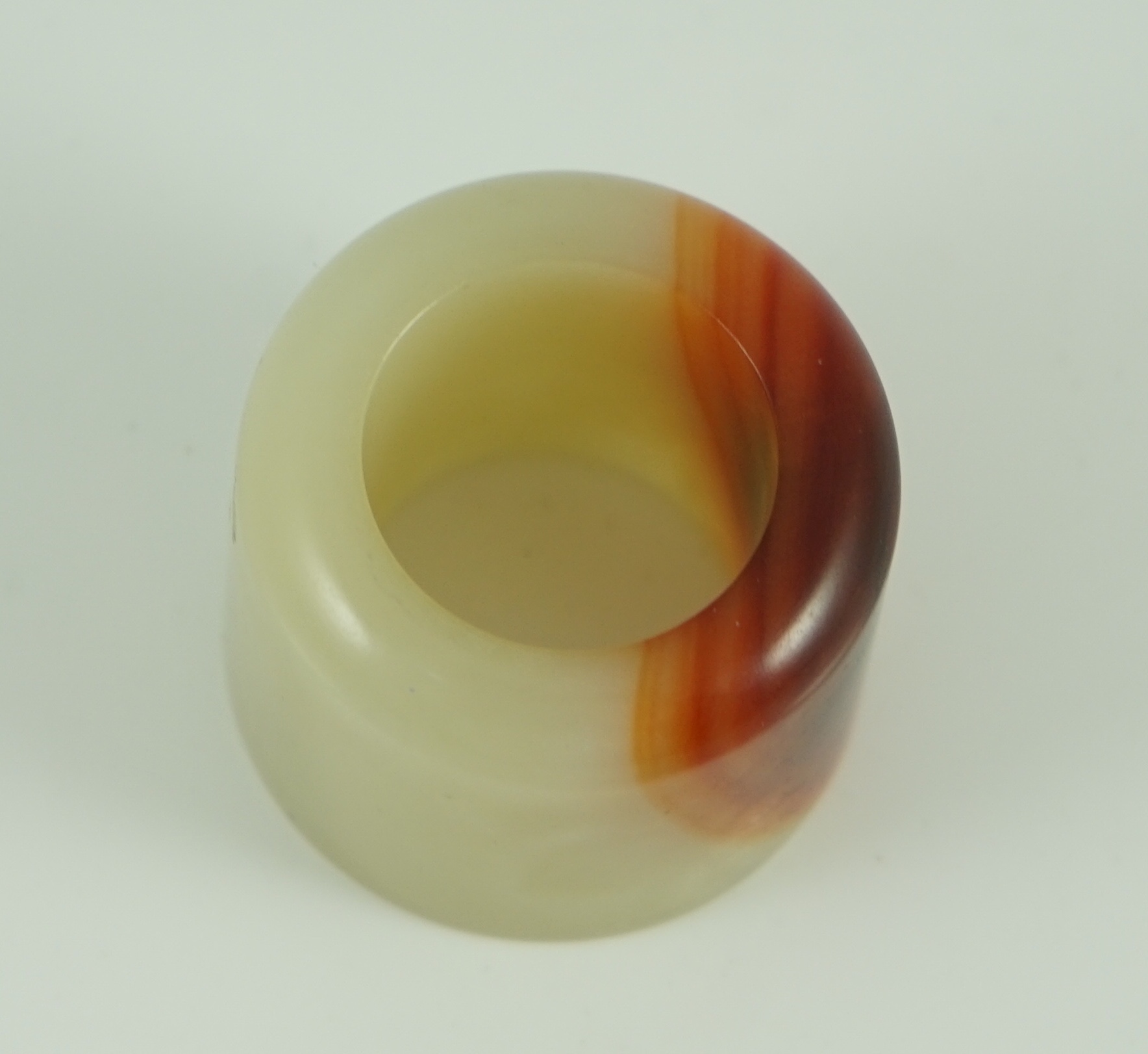 A Chinese pale celadon and russet jade archer's ring, early 20th century 3.4 cm diameter